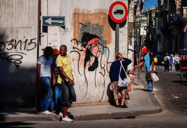 Personas caminan por una calle de La Habana frente a un grafiti, representando la cotidianidad en Cuba durante la aplicación de las nuevas tarifas para trámites de extranjeros.