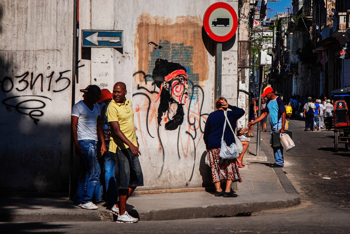 Personas caminan por una calle de La Habana frente a un grafiti, representando la cotidianidad en Cuba durante la aplicación de las nuevas tarifas para trámites de extranjeros.