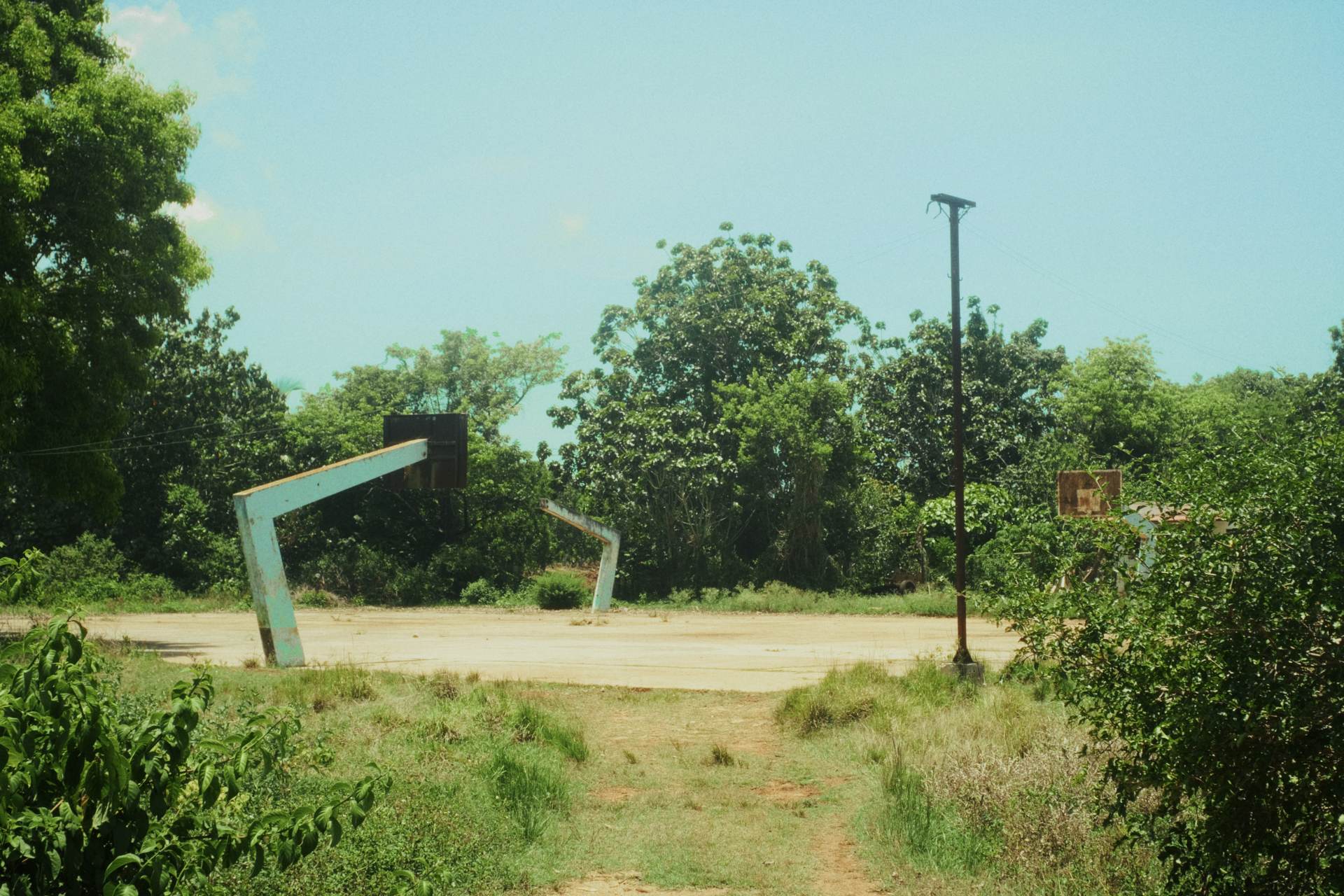 Cancha de baloncesto al aire libre en Ceiba 1, con tableros oxidados y rodeada de vegetación.