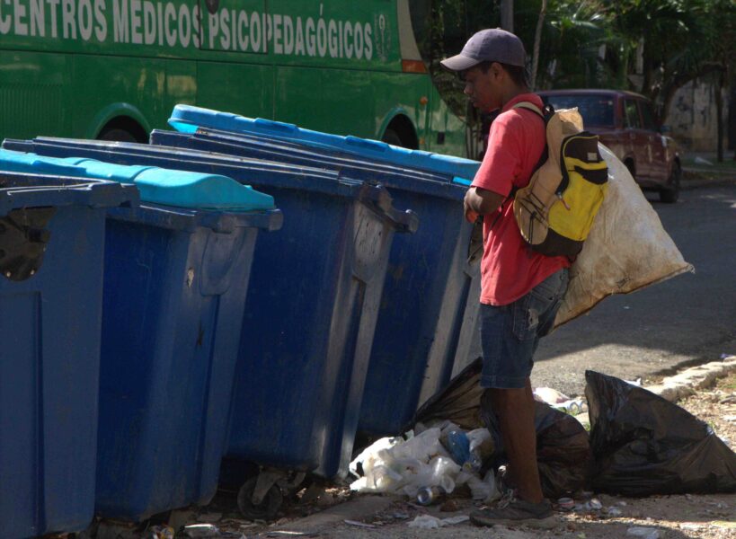 Joven con gorra y mochila revisa una fila de contenedores azules en una calle de Cuba.