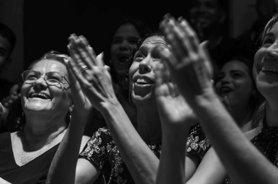 El público de un teatro, visto desde el escenario, aplaude con entusiasmo en la oscuridad.