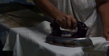 Manos planchando con plancha antigua, rutina de madre soltera.