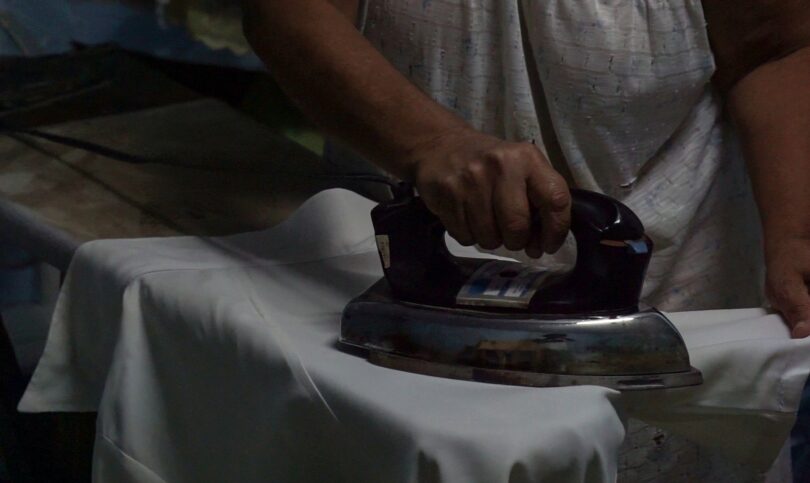 Manos planchando con plancha antigua, rutina de madre soltera.