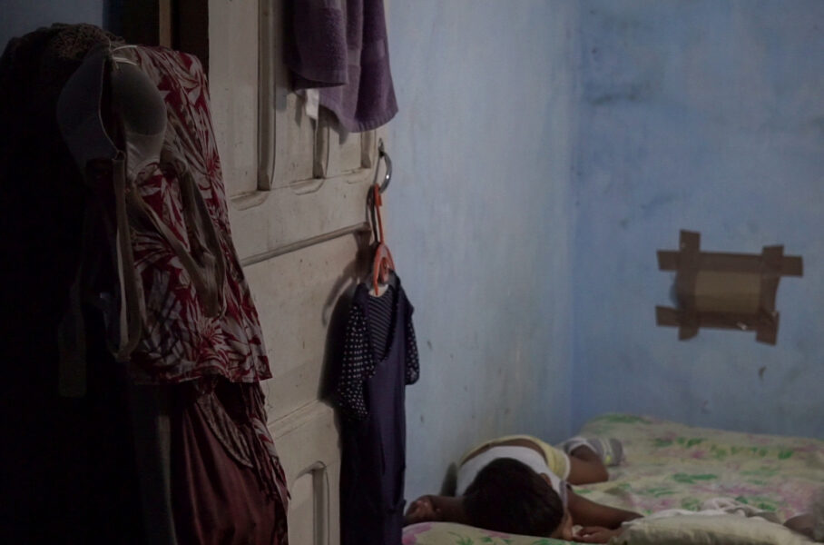 Niño durmiendo en un cuarto pequeño con ropa colgada. Falta de espacio.