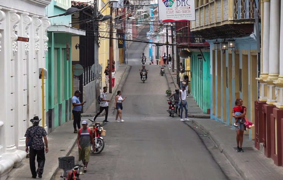Vida cotidiana en Santiago de Cuba. Personas caminan y esperan en una calle concurrida.