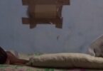 Hacinamiento en Santiago de Cuba. Dos personas (un niño y una adulta mayor) duermen en una cama estrecha en un cuarto pequeño y oscuro, simbolizando el agotamiento de una madre soltera en Cuba.