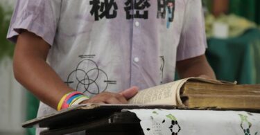 Grupo de hombres rodean a una persona en el centro, colocando sus manos sobre su espalda y hombro en gesto de apoyo y consuelo durante un acto religioso