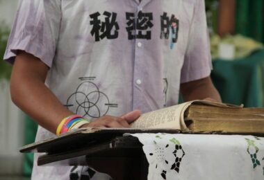 Grupo de hombres rodean a una persona en el centro, colocando sus manos sobre su espalda y hombro en gesto de apoyo y consuelo durante un acto religioso