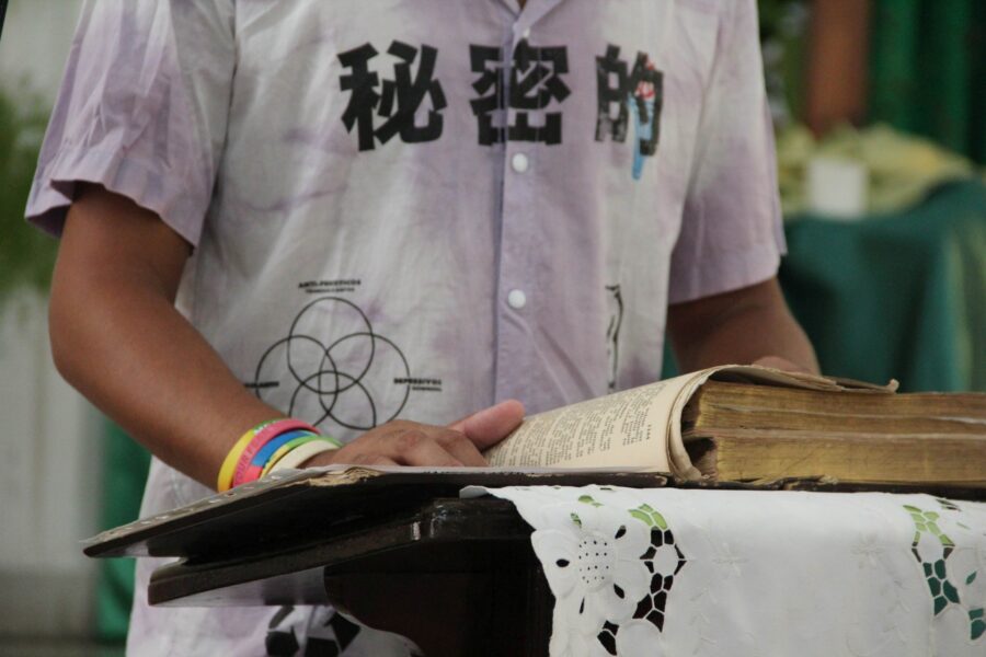 Grupo de hombres rodean a una persona en el centro, colocando sus manos sobre su espalda y hombro en gesto de apoyo y consuelo durante un acto religioso