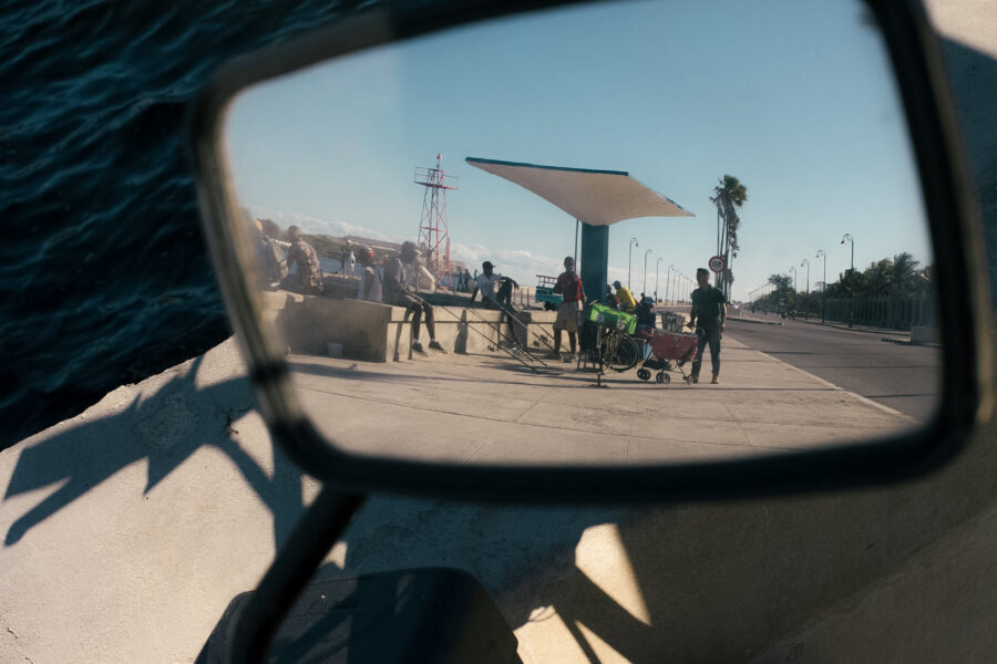 Pescadores y vendedor ambulante en la Avenida del Puerto vistos desde el retrovisor de una moto eléctrica. 