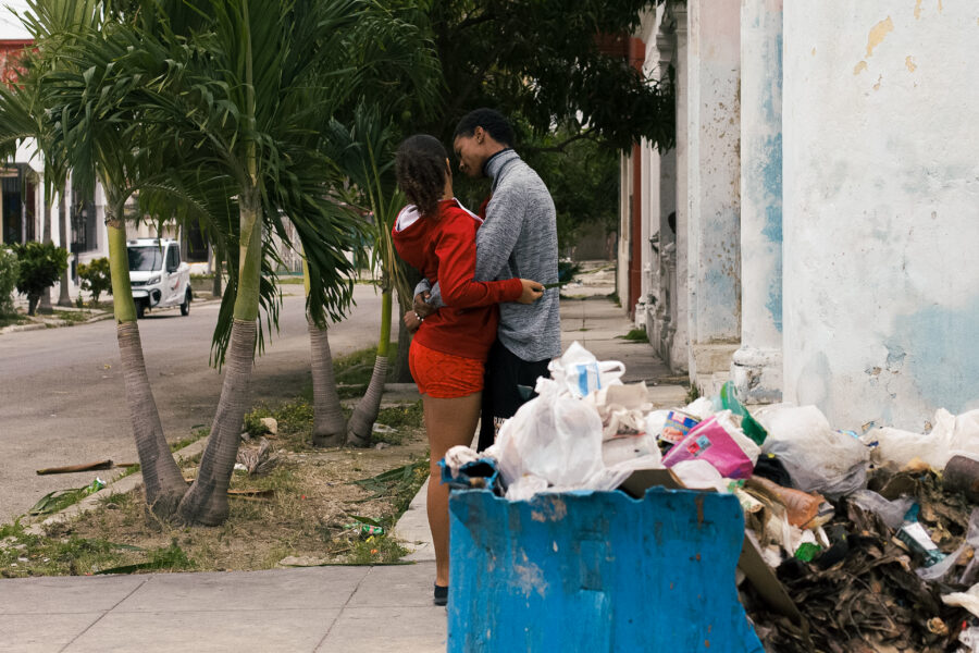 Pareja se besa frente a basurero roto que lleva días sin ser recogido. 