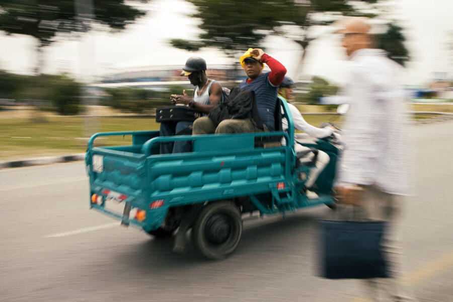 Trabajadores vuelven a sus casas en triciclo eléctrico mientras otro cruza la calle. 