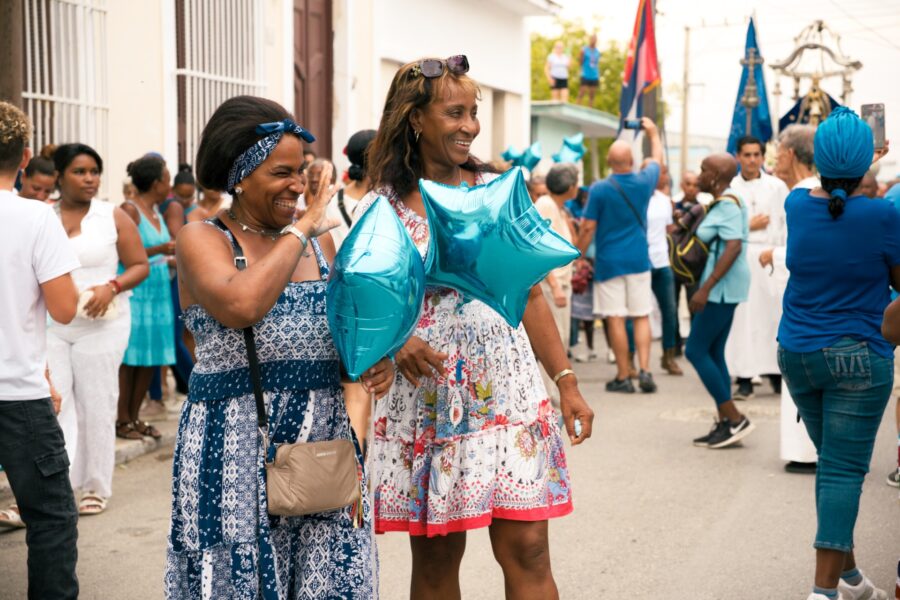 Dos mujeres saludan a vecinos mientras participan de la procesión de la Virgen de Regla. Foto: Neus Pechero.